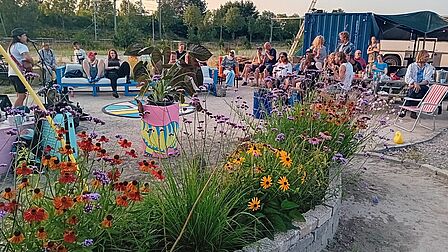 Een tuin met mensen die kijken naar een optreden van iemand met een gitaar