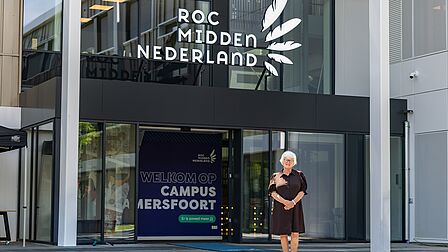 Een vrouw voor de ingang van het gebouw van het ROC.
