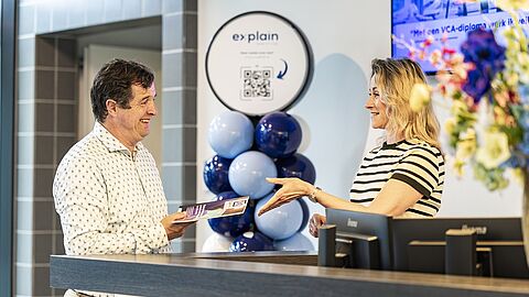 Rob staat naast een balie, waarachter een collega staat