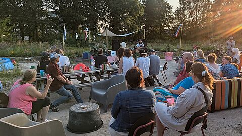 Mensen zitten op stoelen en kijken naar een optreden van een zanger met gitaar. 