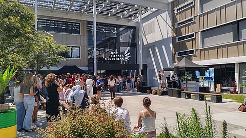 Een grote groep studenten bij de ingang van het gebouw, waarbij iemand een speech geeft.