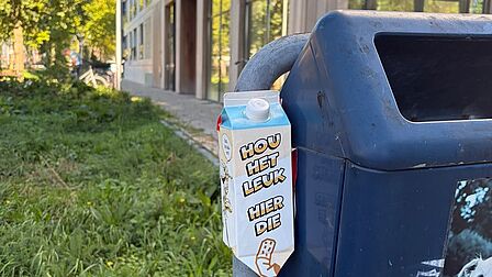 Een drinkpak die hangt tegen een prullenbak aan. De tekst op het pak luidt: 'Houd het leuk, hier die peuk'