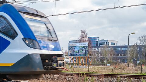 Een trein rijdt langs het bouwbord van Hoefkwartier